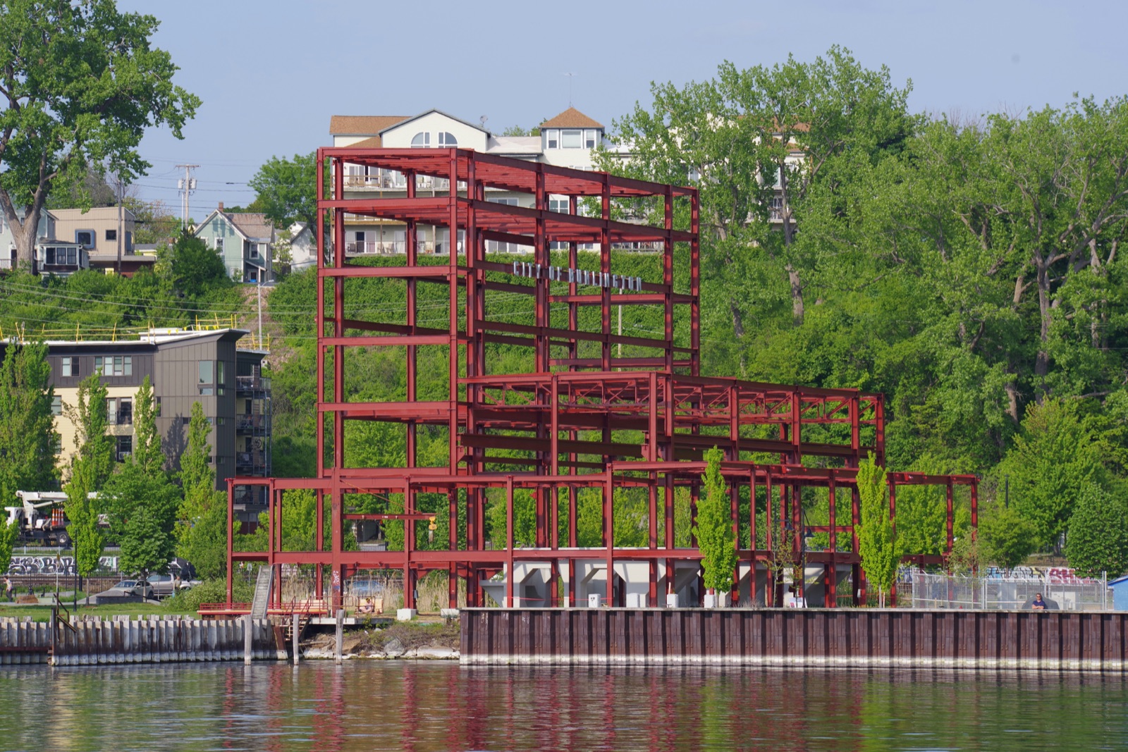 The red steel Moran Frame beside the Burlington waterfront, surrounded by green trees